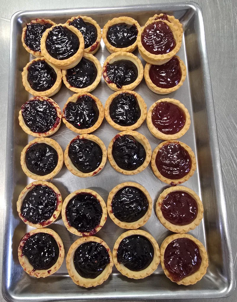 Crostatine mignon alla confettura, in file su un vassoio d'acciaio